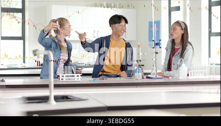 Holding test tube, three students wearing goggles, casual clothes conducting labwork in school lab Stock Photo