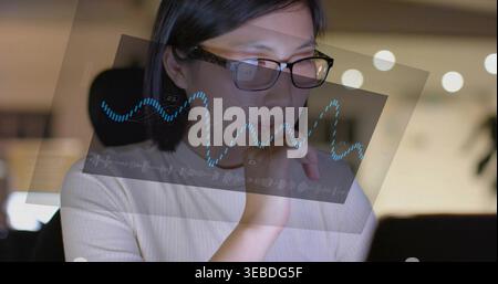 Analyzing woman scanning data at laptop, wearing glasses, ribbed top with blue waveform overlay Stock Photo