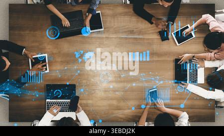 A diverse business team collaborates using digital devices on a wooden table. Dynamic data visualization and technology enhance their brainstorming Stock Photo