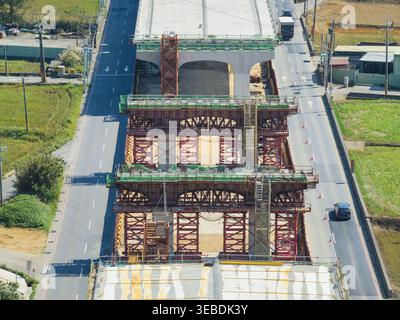 Aerial view of elevated highway construction with steel scaffolding and concrete pillars between active road lanes in Taiwan. Stock Photo