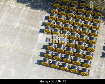 Aerial view of rows of industrial cable reels with yellow rims and black cables neatly arranged on a concrete storage yard in Taiwan. Stock Photo
