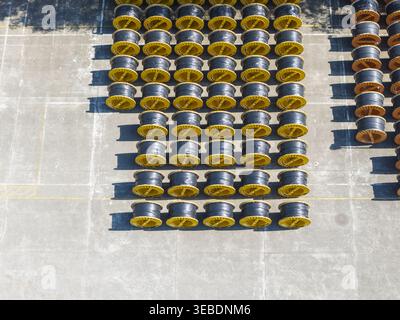 Aerial view of rows of large black cable reels with yellow rims neatly organized on a concrete industrial yard in Taiwan. Stock Photo