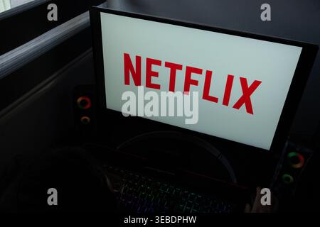 The Netflix streaming service logo shown on a widescreen monitor with a backlit RGB mechanical keyboard and gaming peripherals in the foreground Stock Photo