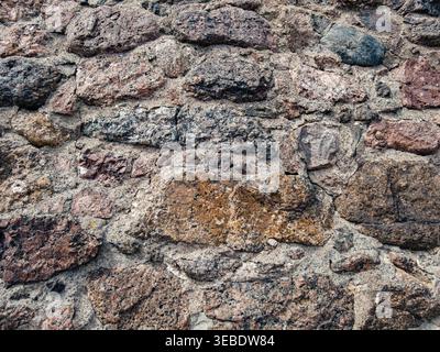 Rough texture of an ancient stone wall showing varied natural colors and weathered mortar outdoors Stock Photo