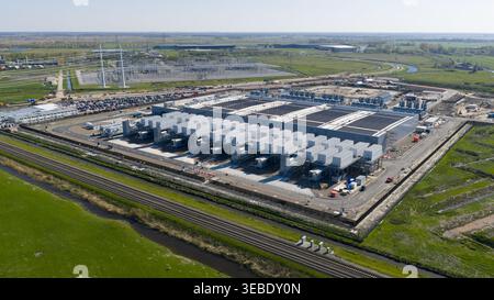 Aerial view of Datacenter Westpoort featuring its large industrial structure with cooling units surrounded by green fields and railway tracks in Groni Stock Photo