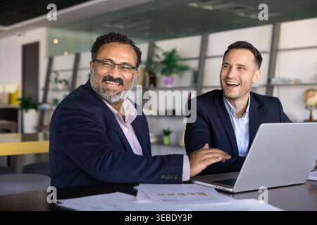 Two laughing businessmen engage in teamwork in modern corporate office Stock Photo