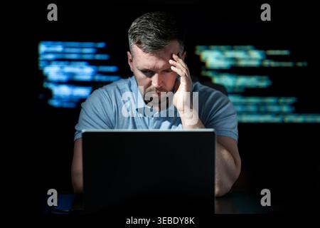 Cybersecurity hacker works on laptop. Cybersecurity hacker analyzes green code. Cybersecurity hacker monitors network threat. Cybersecurity hacker Stock Photo