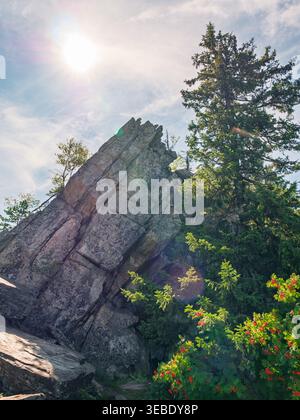 Sun shines brightly over a massive rock cliff, casting light on rugged surfaces. Stock Photo