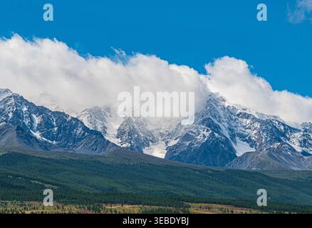 Snow-capped peaks of Altai mountains rise majestically under a clear blue sky with white clouds Stock Photo