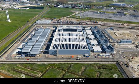 Aerial view of Datacenter Westpoort featuring a large industrial building with solar panels on the roof surrounded by green fields and power infrastru Stock Photo