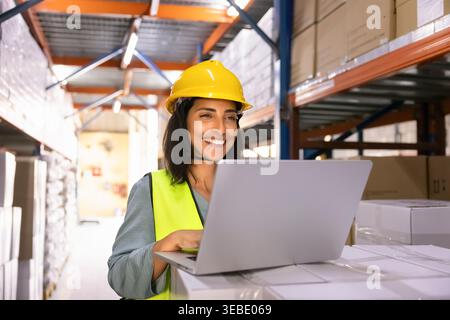 Smiling female logistics worker using laptop in warehouse Stock Photo