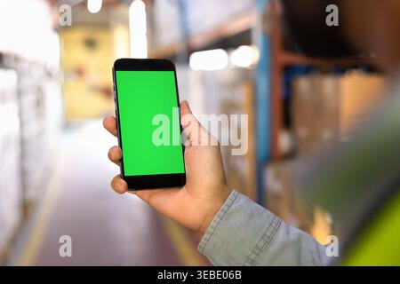 Male worker holding smartphone with green screen in warehouse facility Stock Photo