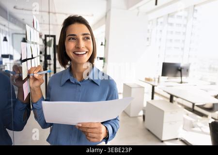 Woman employee organizing tasks on office glass wall Stock Photo