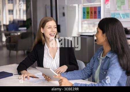 Two young professional women talking seated at desk in boardroom Stock Photo