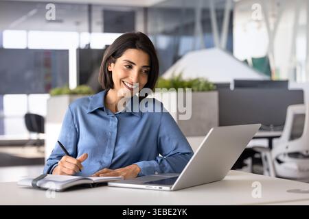 Woman watching educational content on laptop, making notes in notebook Stock Photo