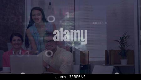 Reviewing three-person team leaning over laptop in meeting room, in pink blazer and denim top Stock Photo