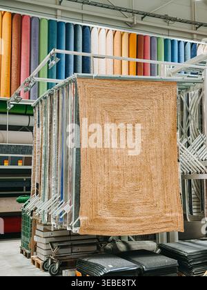 Valmiera, Latvia - April 22, 2026:Modern carpet showroom interior featuring hanging rug samples and vibrant rolls on display racks. Ideal for retail, Stock Photo