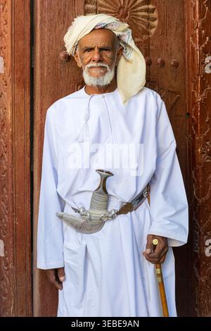 An elderly gentleman in traditional Omani attire with a turban, collarless robe, a highly decorated dagger and cane in Nizwa, Oman Stock Photo