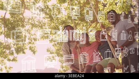 Swinging family wearing shorts and striped top on wooden swing under tree, showing overlay icons Stock Photo