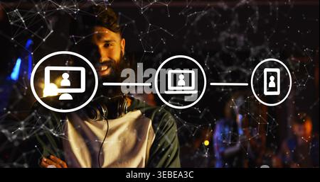 Smiling bearded man standing in dim event venue, wearing raglan tee with headphones, network icons Stock Photo