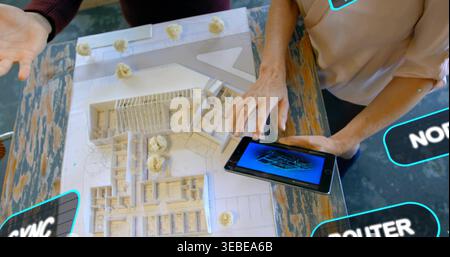 Examining white scale model, two designers touching 3D tablet in design studio, wearing pink blouse Stock Photo
