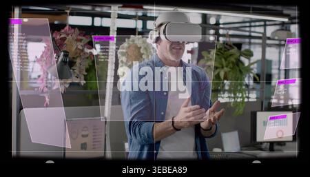 Gesturing mature man wearing denim shirt, white VR headset manipulating AR panels in open office Stock Photo