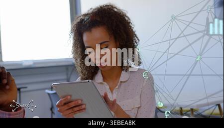 Using tablet, woman in dotted blouse tapping screen at office, network overlay and left arm visible Stock Photo