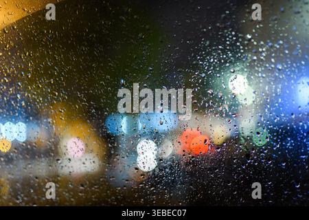 Raindrops on window with blurred city bokeh lights at night, rainy urban mood with selective focus Stock Photo