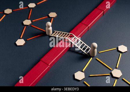 Wooden figures connected by ladder bridging red barrier between network nodes. Concept of solution, connection, and overcoming division in structured Stock Photo