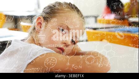 Resting schoolgirl in white top leaning on folded arms at desk in classroom with formulas overlay Stock Photo