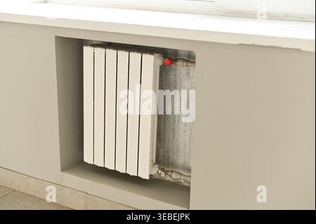 Wall-mounted radiator installed under window in indoor space, heating unit with white panels, interior detail of modern building, heating battery prov Stock Photo