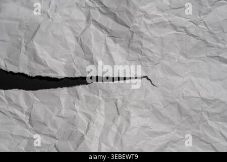 Abstract background of wrinkled white paper with a jagged tear showing black background, close up. Concept of revealing hidden information opening a g Stock Photo