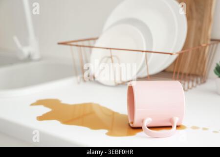 Overturned cup and spilled coffee on counter in kitchen, closeup Stock Photo