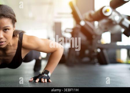 Closeup of determined young Black woman doing push-ups on gym floor Stock Photo
