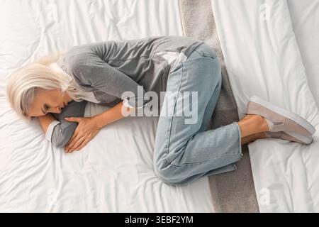 Depressed mature woman lying on bed, top view Stock Photo