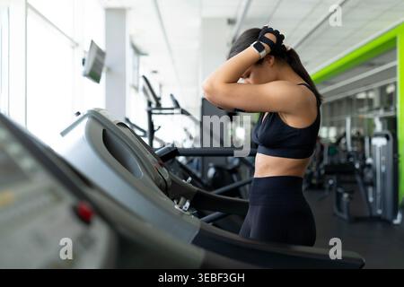 Young Black woman standing on treadmill with hands behind head looking exhausted Stock Photo