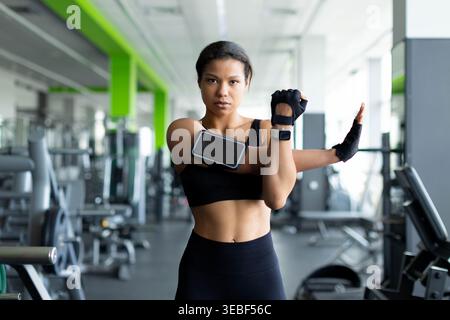 Young black woman stretching arm muscles in gym wearing armband phone holder Stock Photo