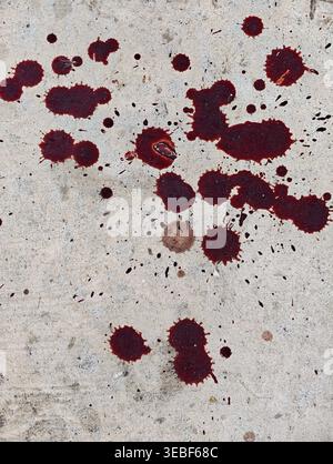 A close up of red and dark brown blood splatters scattered across a concrete surface The scene has a macabre or crime related mood suitable for horror Stock Photo