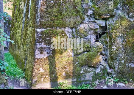 A weathered, moss-covered stone and concrete wall, likely part of an old military bunker or fortress ruin. The structure shows significant aging with Stock Photo
