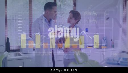 Pointing dentist in lab coat and clinician in tunic by dental chair analyzing tablet, data overlay Stock Photo