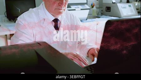 Typing technician in white lab coat and dark tie working on laptop at print room, copier Stock Photo