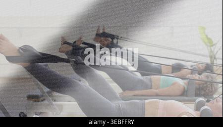 Lying three women in sportswear performing legwork on pilates reformers in studio, with straps Stock Photo
