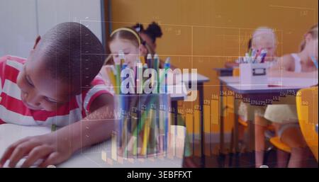 Leaning boy in red striped shirt writing in classroom, clear cup of colored pencils, copy space Stock Photo