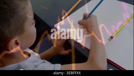 Writing boy in gray tee holding blue pencil and stabilizing paper at desk with chart overlay Stock Photo