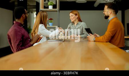 Two business professionals connect through a handshake at a stylish office table while colleagues observe, excited about the new collaboration ahead. Stock Photo