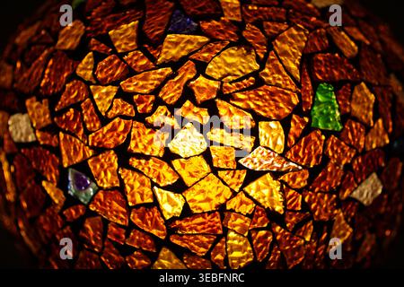Close-up of colorful mosaic glass texture with warm light, glowing amber and gold stained glass fragments for decorative artistic background. Stock Photo