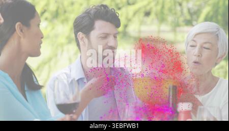 Holding woman in light blue top raising red wine glass at garden table, magenta powder erupting Stock Photo