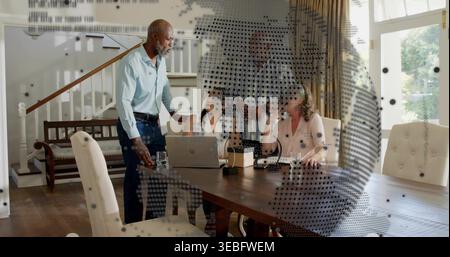 Discussing group of four in business-casual leaning around wooden table at home, with laptop Stock Photo