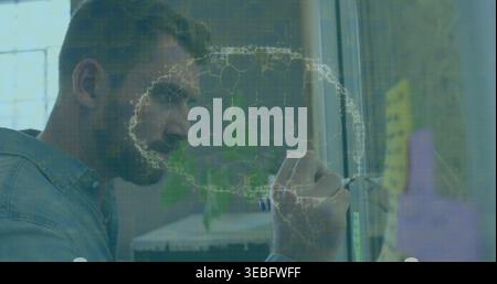 Writing senior man wearing denim shirt on glass partition at office with marker and sticky notes Stock Photo