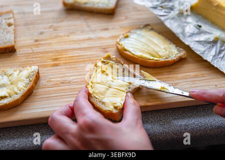 Butter bread sandwich with female woman hand spreading dairy fat with knife on wooden cutting board at home kitchen macro closeup Stock Photo